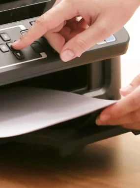 Mão ajustando configurações em impressora enquanto outra mão segura papel para impressão.