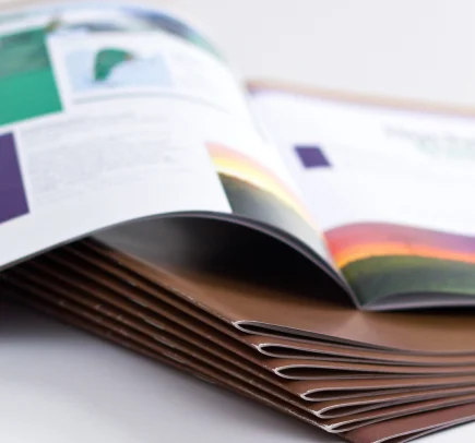 Pilha de revistas abertas mostrando páginas coloridas com textos e imagens, destacando a dobra das folhas.
