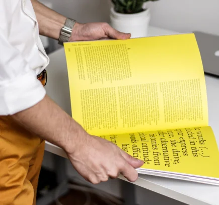 Pessoa lendo uma revista com páginas amarelas em um ambiente de escritório.