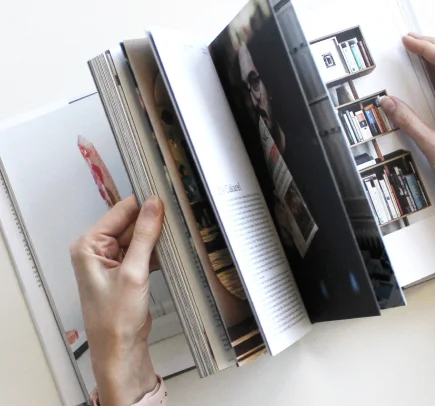 Mãos folheando um livro com páginas que mostram fotos e textos sobre arte e design.