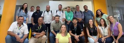 Grupo de dezesseis pessoas sentadas e em pé, sorrindo em ambiente interno com paredes amarelas e branco.
