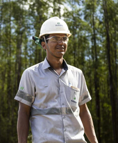Trabalhador usando capacete branco e óculos de segurança em ambiente florestal.
