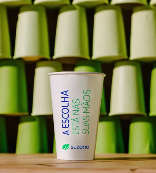 Copo branco com texto "A ESCOLHA ESTÁ NAS SUAS MÃOS" e logo da �ڰ������� em fundo de copos verdes empilhados.