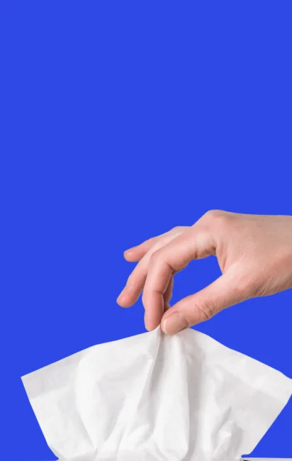 Mão segurando um lenço de papel branco contra fundo azul.