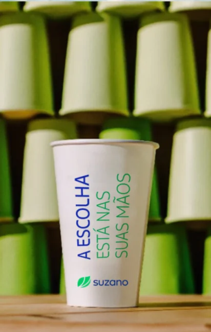 Copo branco com o texto azul e verde "A ESCOLHA ESTÁ NAS SUAS MÃOS" da �ڰ�������, com copos verdes empilhados ao fundo.
