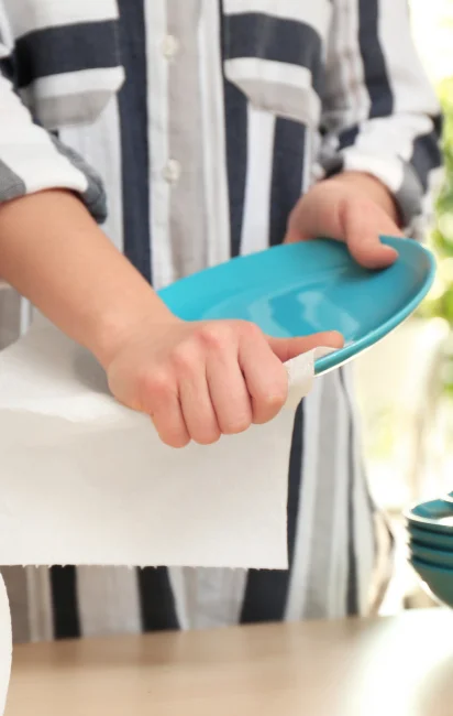 Pessoa segurando um prato azul e limpando-o com papel toalha branco em uma bancada de madeira.