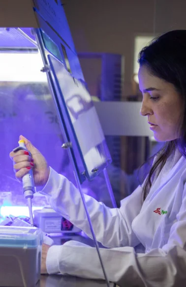 Mulher cientista usando jaleco branco manuseando micropipeta em laboratório com luz azul.