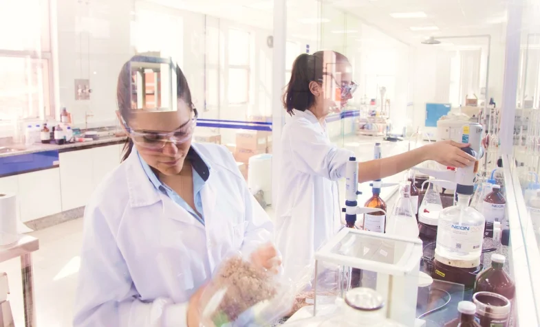 Duas mulheres com jalecos brancos realizando experimentos em um laboratório científico iluminado.