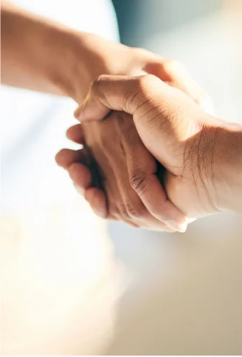 Duas mãos entrelaçadas em gesto de apoio e solidariedade com fundo desfocado.