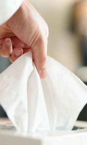 Uma mão puxando um lenço branco de uma caixa de lenços descartáveis.