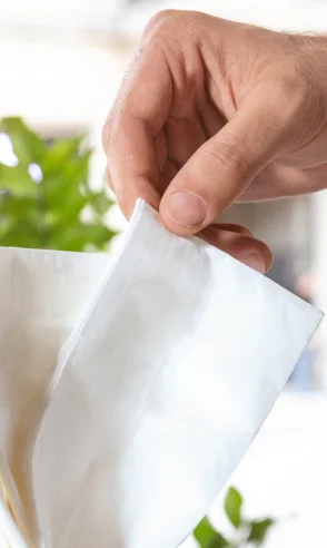 Mão masculina puxando um lenço branco de uma embalagem transparente.
