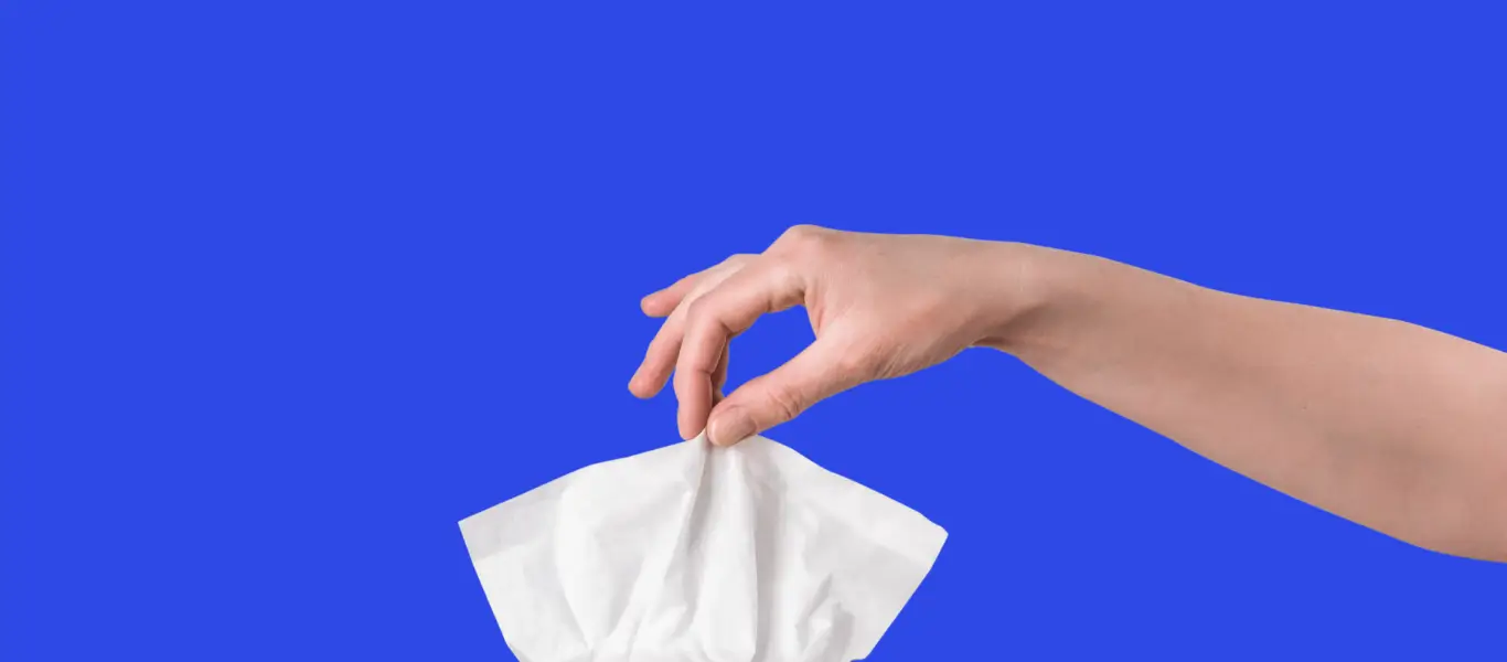 Mão segurando um lenço de papel branco contra fundo azul.