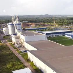 Vista aérea de uma fábrica industrial com silos, edifícios longos e áreas verdes ao redor.