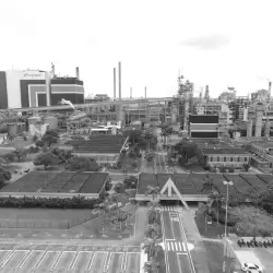 Vista aérea em preto e branco de uma fábrica com várias construções, chaminés e áreas arborizadas.