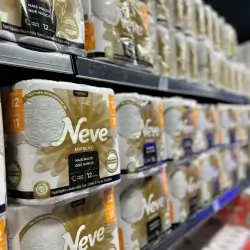 Pacotes de papel higiênico da marca Neve empilhados em prateleiras de supermercado.