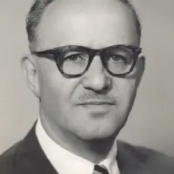 Retrato em preto e branco de um homem de meia-idade usando óculos, terno e gravata.