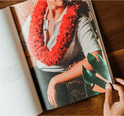 Pessoa segurando um livro aberto que mostra a imagem de uma pessoa usando uma blusa branca e um colar de flores vermelhas.