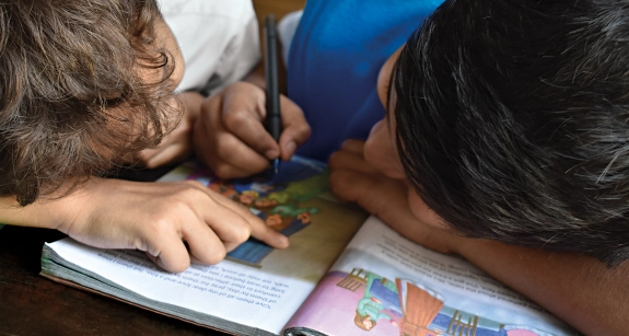 Duas crianças lendo e interagindo com um livro ilustrado aberto sobre a mesa.