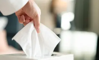 Mão puxando um lenço de papel branco de uma caixa.