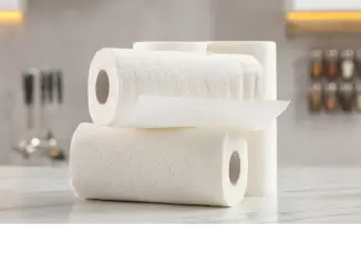 Três rolos de papel toalha branco empilhados sobre uma bancada de cozinha clara.