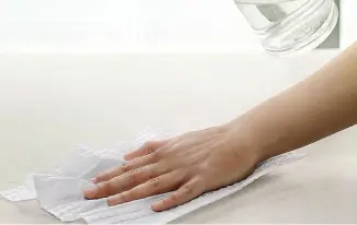 Mão limpando uma superfície branca com um pano úmido próximo a um copo de vidro.
