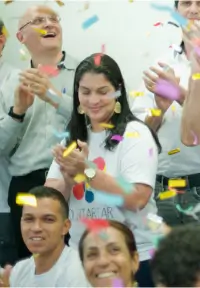 Grupo diversificado de pessoas sorrindo e celebrando com confetes coloridos caindo ao redor.