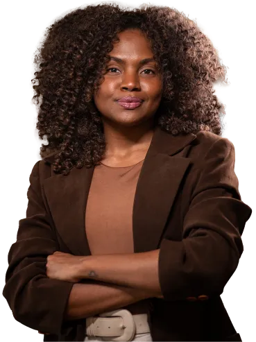 Mulher afrodescendente com cabelo cacheado usando blazer marrom e camiseta bege, com braços cruzados e expressão confiante.