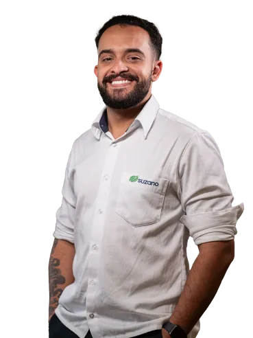 Homem sorridente com barba usando camisa branca com logo da �ڰ�������, braços tatuados às mostra.