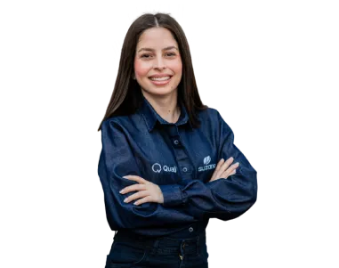 Mulher sorridente com cabelos lisos castanhos escuros, vestindo camisa azul escura com braços cruzados.
