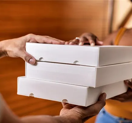 Duas pessoas trocando uma pilha de três caixas retangulares brancas, possivelmente de pizza.