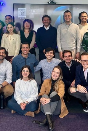 Grupo diversificado de pessoas sorrindo e posando para uma foto em um ambiente de escritório moderno.