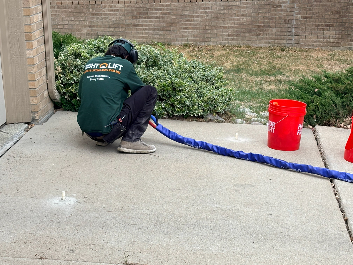 Worker in a green RightLift shirt crouched on a concrete driveway using equipment for concrete lifting and leveling injecting.