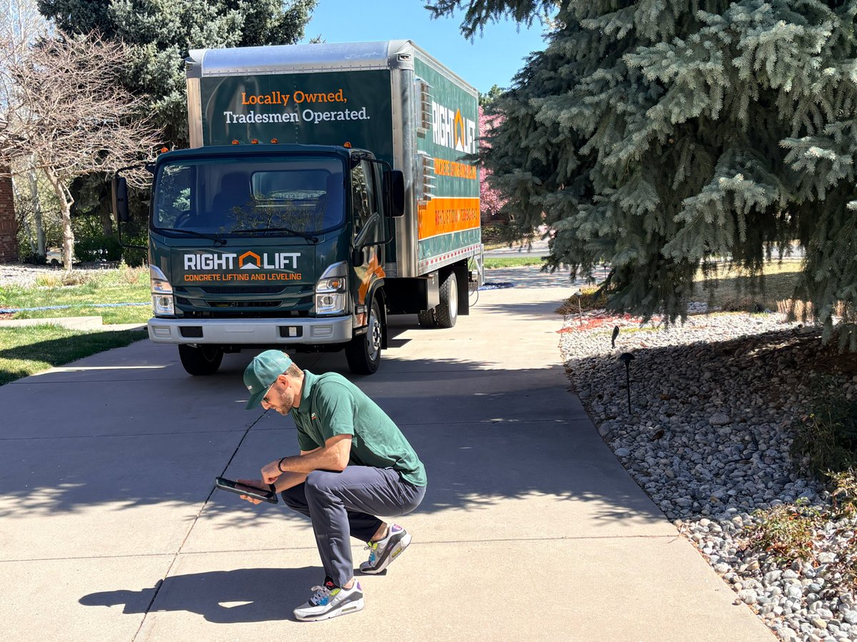 Tradesmen squatting on a driveway using a tablet in front of a RightLift concrete lifting and leveling truck.
