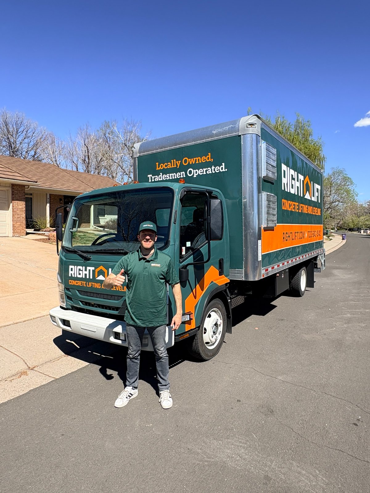 Tradesmen in green RightLift uniform giving a thumbs-up standing in front of a green and orange RightLift concrete lifting and leveling service truck on a residential street.