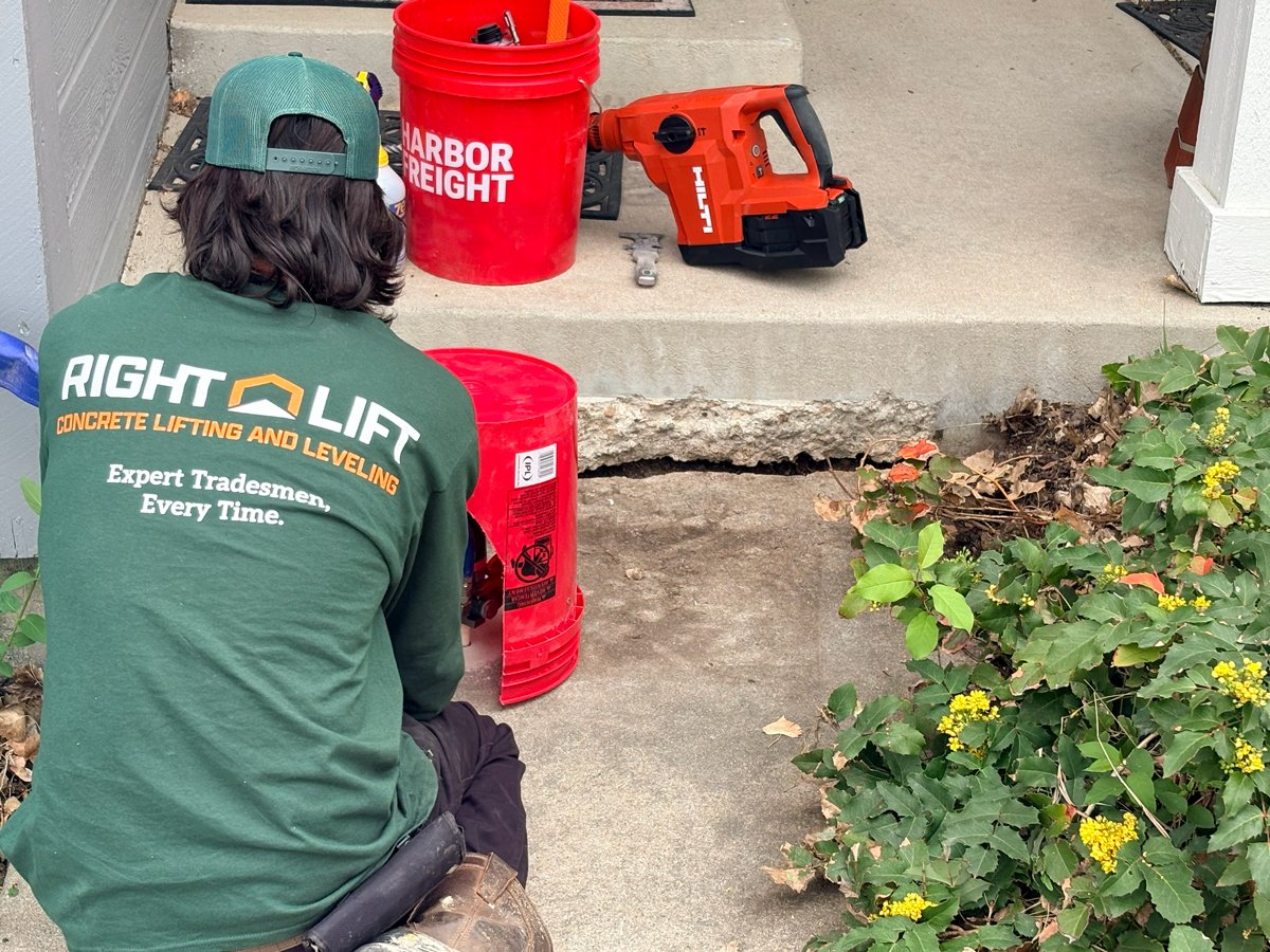 Tradesmen wearing a green RightLift shirt kneeling on a concrete surface with an exposed cracked concrete slab and tools nearby.