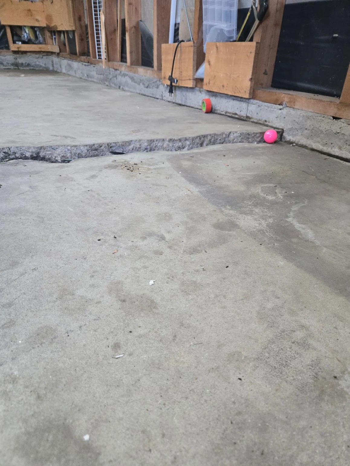 Residential concrete garage floor with a large crack near a wooden wall frame.