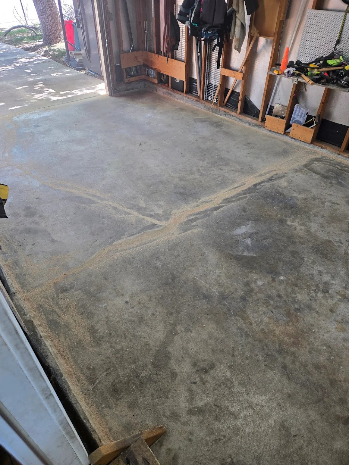 Empty garage with a cracked concrete floor and exposed wall studs with hanging tools and jackets.