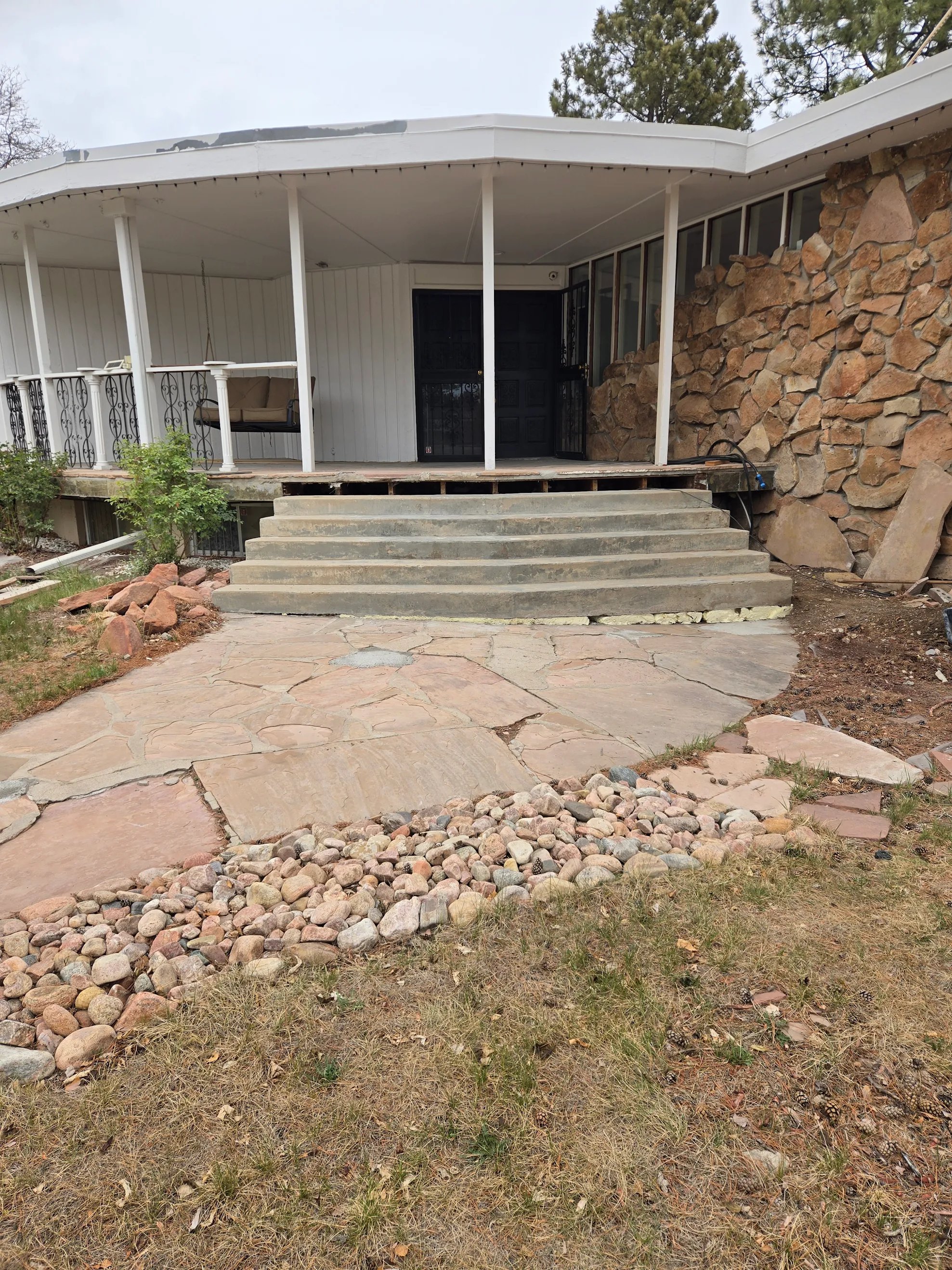 Repaired stone patio with concrete steps leading to porch of house with stone wall and porch swing.