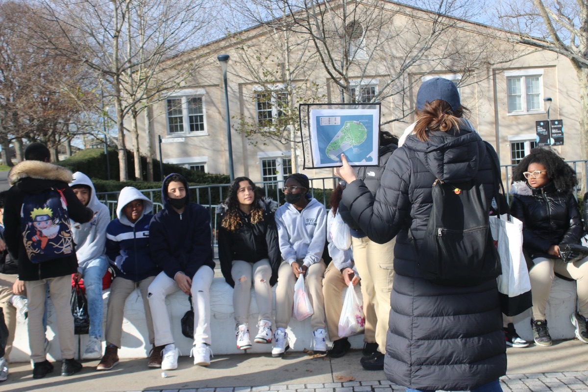 A guide holds a map of Governors Island while students gather outside New York Harbor School