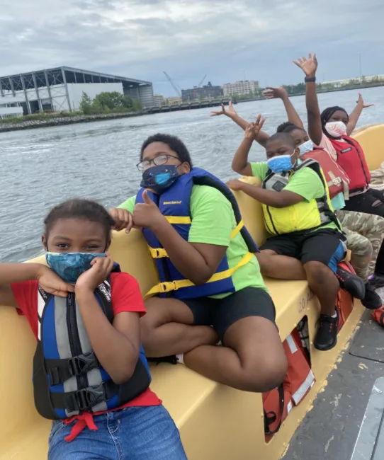 Young people wearing life jackets celebrate together aboard a boat