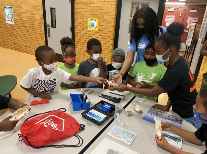 Students use tablets and testing supplies around a classroom table