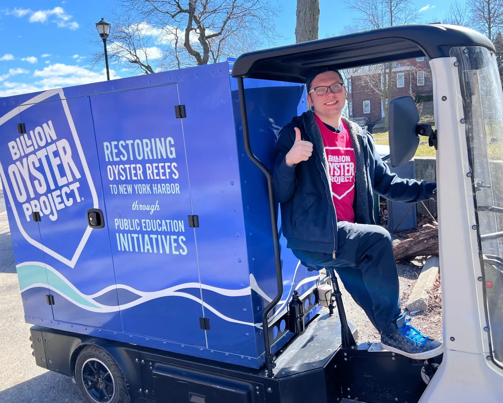 A Billion Oyster Project staff member gives a thumbs-up from a branded utility vehicle