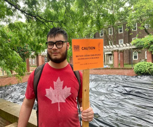 Student holds a caution sign on a flooded Governors Island path