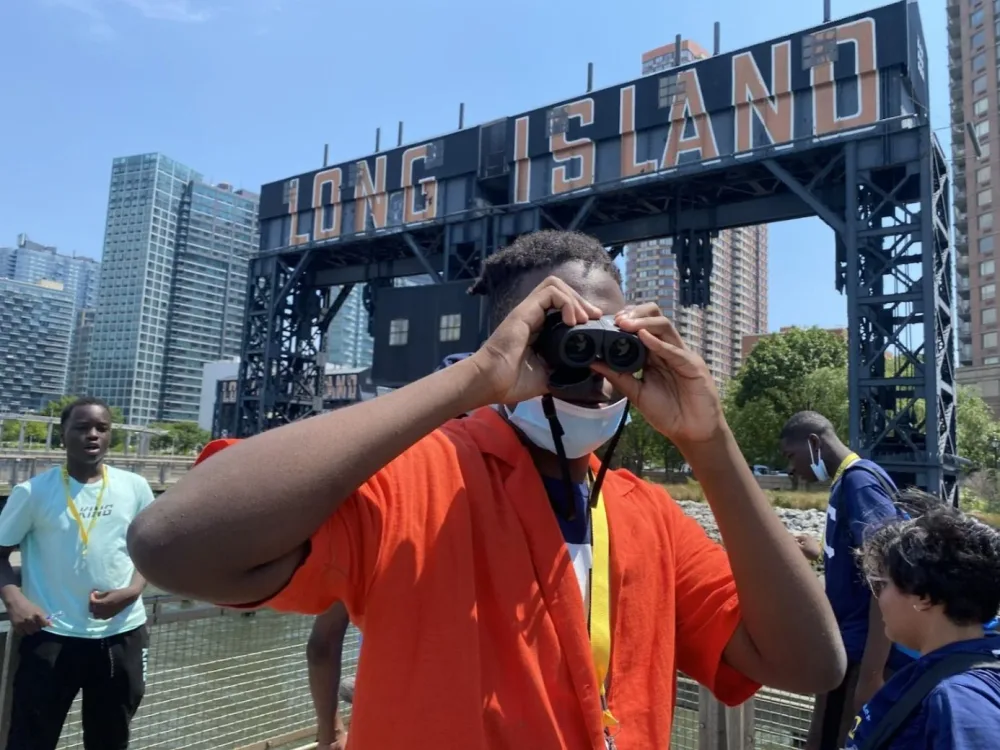 Participant uses binoculars beneath the Long Island sign
