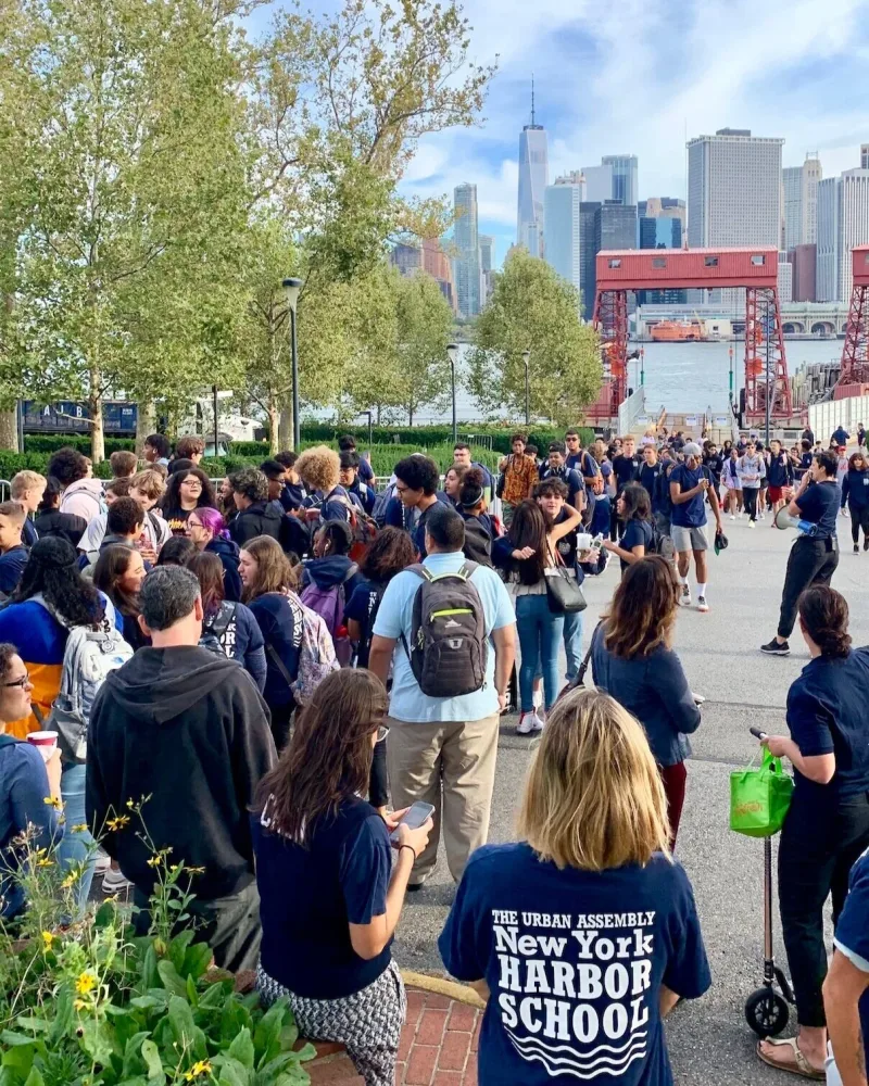 Harbor School students crowd the Governors Island waterfront on the first day, Lower Manhattan across the water.