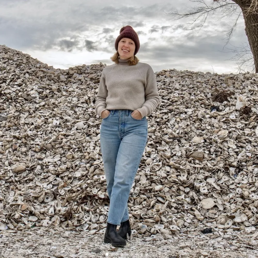 Team member stands on a mound of recycled oyster shells