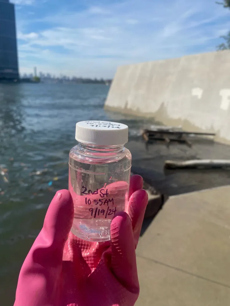 Volunteer holds a jar of harbor water with the skyline behind her