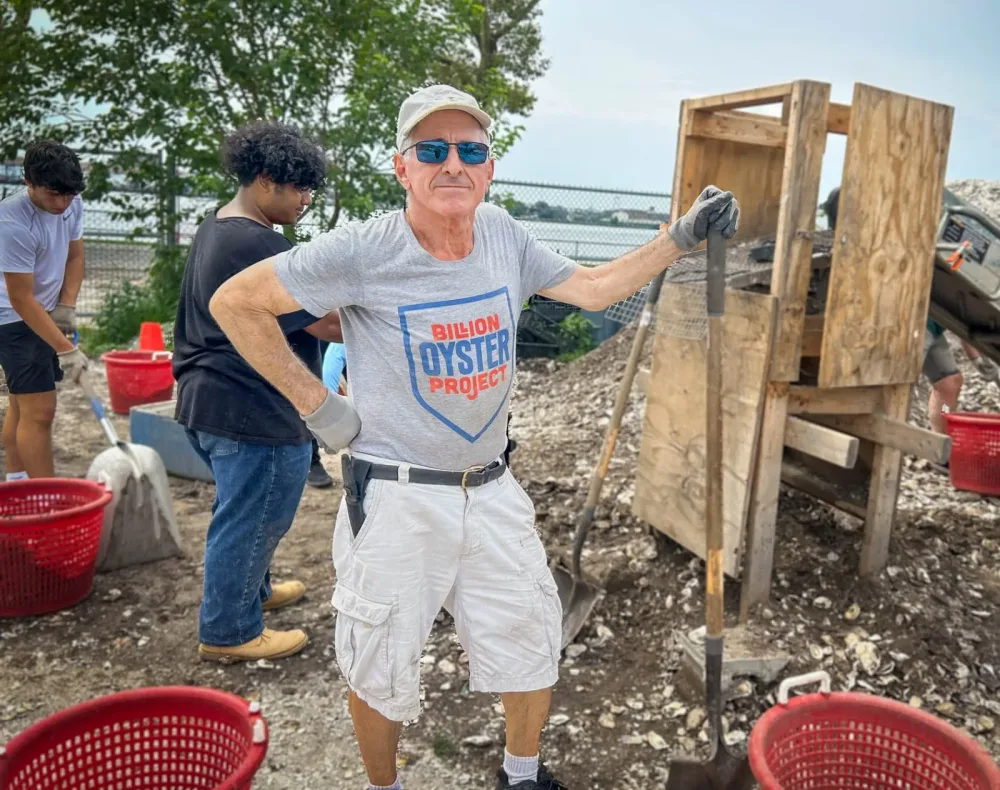 Volunteer stands beside buckets at a recycled-shell work site