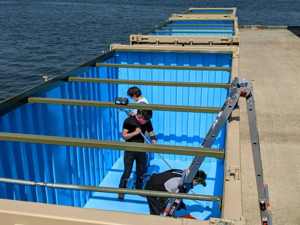 Workers tend rows of blue outdoor oyster tanks