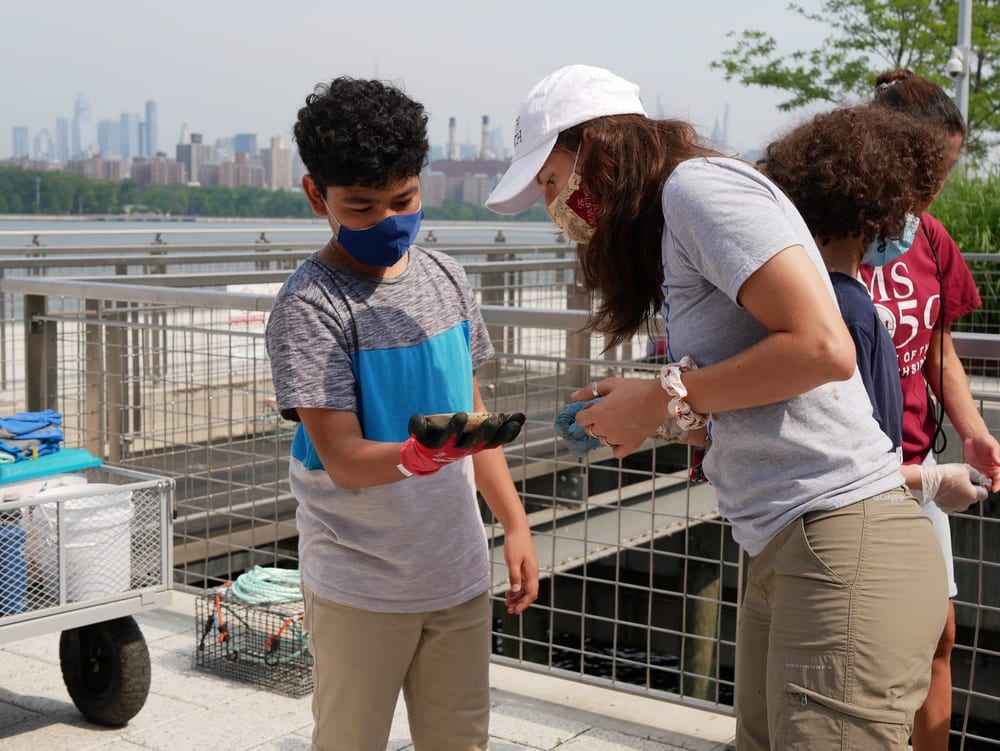 Student and educator examine an oyster cage beside the waterfront